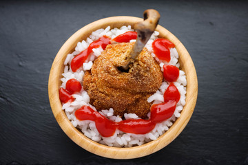 Breaded chicken leg with rice and ketchup, in a wooden bowl