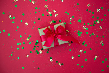 gift box on golden sequins and stars red background. Top view, flat lay. Copyspace for text. Festive holiday background.