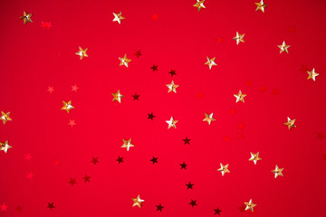 red sparkling sequins stars on red background. Top view, flat lay. Copyspace for text. Bright and festive holiday background.