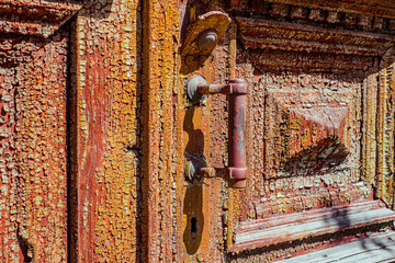 Metal handle on the old wood door, painted old green with peeling paint and red layer under it. Horizontal texture