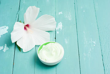 cosmetic cream and white mallow flower on blue wood table
