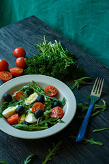 Greek salad with fresh tomatoes, arugula, eggs, olives with olive oil on a dark wood background. Healthy food. Veggie dish.