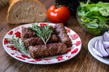Barbeque Kebab, traditional middle eastern and mediterranean eat from minced meat on the grill with lettuce, tomato and red onion on wooden table.