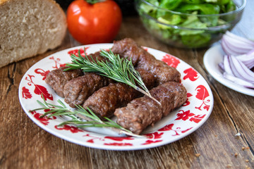 Barbeque Kebab, traditional middle eastern and mediterranean eat from minced meat on the grill with lettuce, tomato and red onion on wooden table.