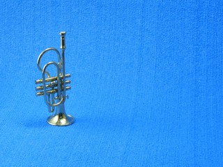 Close-up of a miniature golden trumpet. There is room for text and captions. Textured blue background.