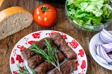 Barbeque Kebab, traditional middle eastern and mediterranean eat from minced meat on the grill with lettuce, tomato and red onion on wooden table.