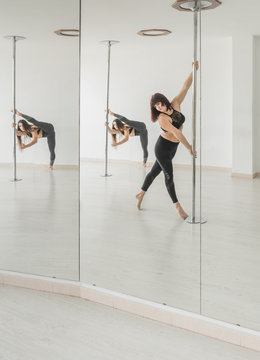 Reflection in mirror of young slim sportive women training near pole in light room
