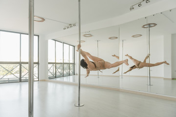 Young slim strong woman practicing on pole in light room studio