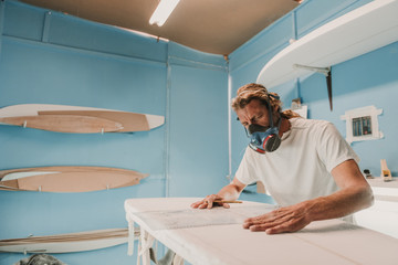 Man in respirator measuring surf board in workshop