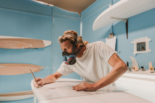 Side view of male in breather holding pencil and measuring surf board in workplace