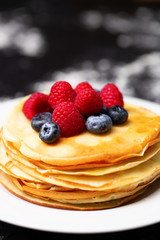 Closeup image of plate of pancakes, blueberries, raspberries and powdered sugar.