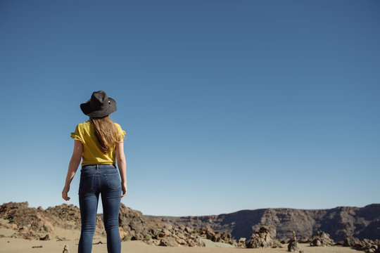 From below woman standing against blue cloudless sky and dry mountains