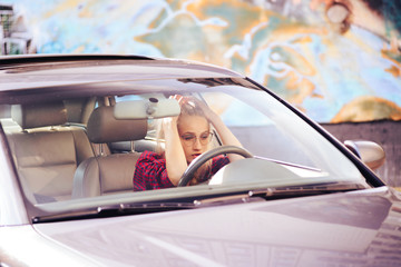 Attractive blonde girl driving a car holding her hand on her head, tired of city traffic jams.