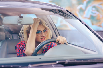 Attractive girl sitting behind the wheel of a car with a dissatisfied look clutching his hand over his forehead.