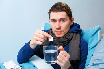 Photo of sick man in scarf with tablet and mug lying in bed