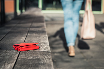 Woman is leaving from a bench where she forgot her leather wallet. Lost purse