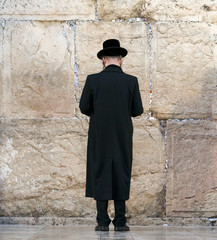 Orthodox hassidic religious jews dressed in black traditional outfit pray at the wailing wall