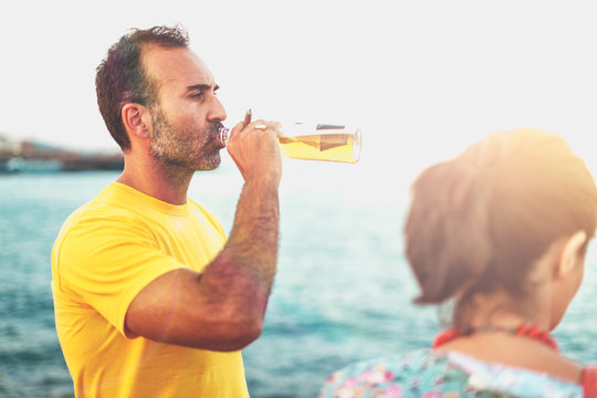 bearded man drinking beer with some friends outdoor watching the sea and smoking a cigar