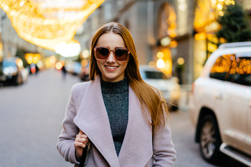 Fototapeta premium Beautiful young caucasian woman standing next standing in luxury district in city downtown. Stylish female model wearing sunglasses photographed in luxury district.