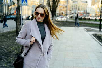 Beautiful young caucasian woman walking along the street in the city. Stylish female model swinging her hair in sunglasses walking on city street.