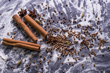 Ingredients for baking dough including flour, sugar, cinnamon, anise star, whisk and rolling pin on dark background.