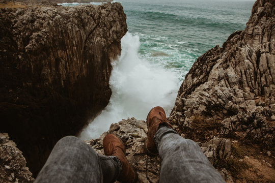Crop legs of human sitting on top of stone near stormy sea in Bufones de Pria, Asturias, Spain
