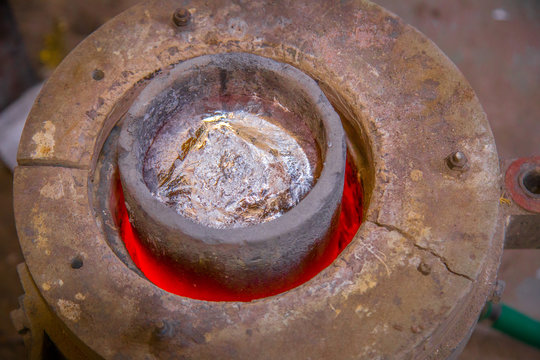 Closeup metal product melting in crucible on little foundry on blurred background