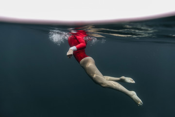 Side view of female in red swimsuit diving in blue water of sea on Bali, Indonesia