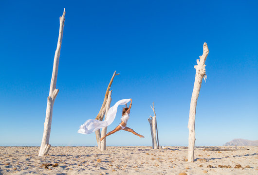 Side view of attractive woman jumping with pareo on sandy beach inn sunny cloudless day