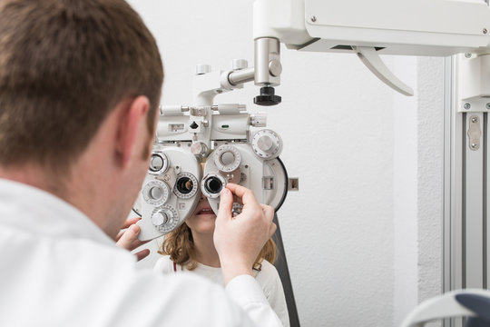 Optician testing a girl's eyes with optometry devices