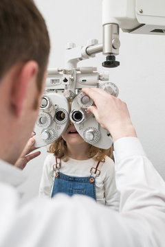 Optician testing a girl's eyes with optometry devices