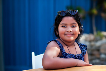 Portrait of a friendly little girl wearing shades and modest clothing while sitting and smiling in an outdoor setting.