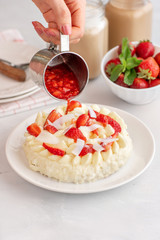 womens hands pour the sauce on the cake. Delicate strawberry cheesecake with coconut. Delicious homemade cake with Fresh berries on light table