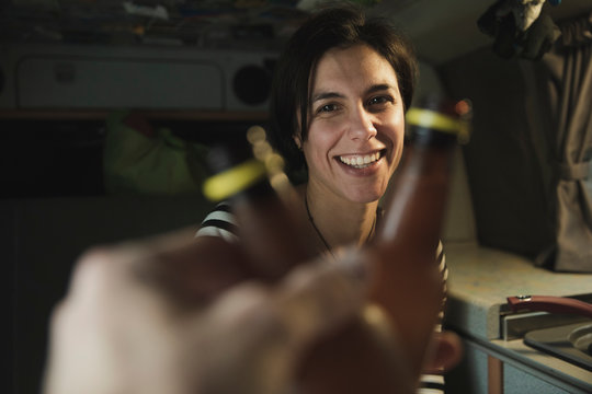 Young brunette cheerful lady clanging bottles with human near electric cooker in mobile home