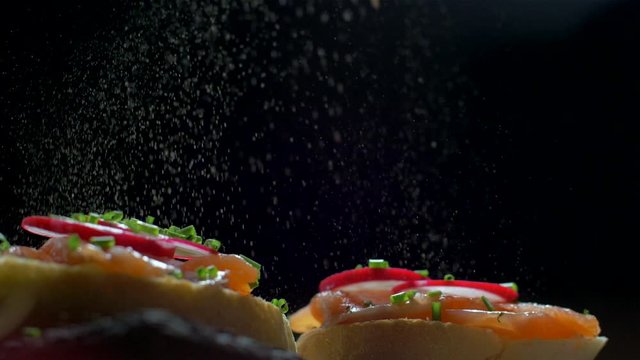 Sprinkling a sandwich with salmon with pepper. Slow motion