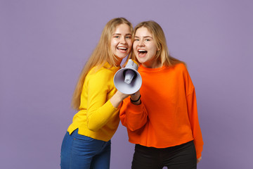 Two cheerful pretty young blonde twins sisters girls in vivid colorful clothes scream on megaphone isolated on pastel violet blue wall background. People family lifestyle concept. Mock up copy space.