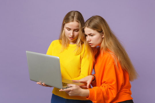Two concerned young blonde twins sisters girls in vivid colorful clothes hold, using laptop pc computer isolated on pastel violet blue background. People family lifestyle concept. Mock up copy space.