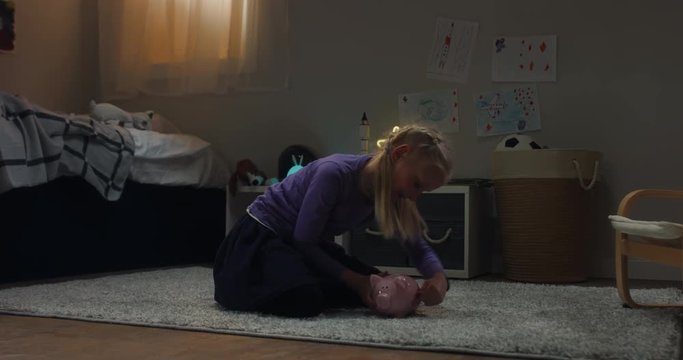 Cute little child girl puts coins into piggy bank in her room, bedroom interior evening shot. 4K UHD RAW FOOTAGE