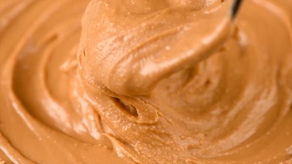 Peanut butter background. Creamy smooth peanut butter in jar backdrop. Mixing with a Spoon, organic food. American cuisine. 4K UHD video, slow motion - Powered by Adobe