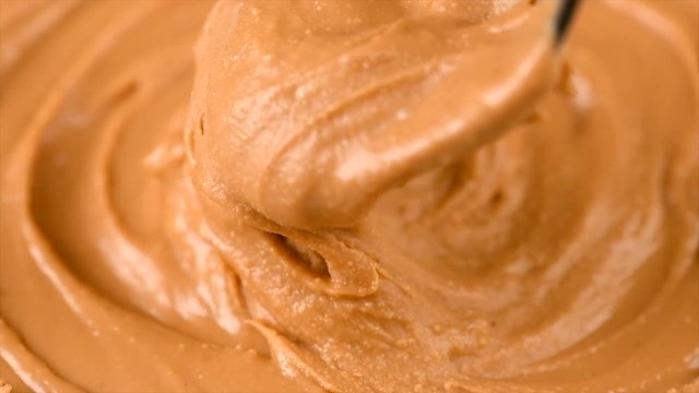 Peanut butter background. Creamy smooth peanut butter in jar backdrop. Mixing with a Spoon, organic food. American cuisine. 4K UHD video, slow motion