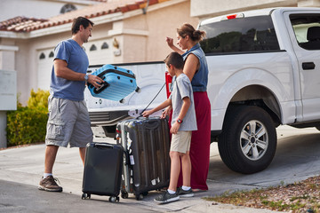Fototapeta na wymiar hispanic family packing luggage into pickup truck in front of house
