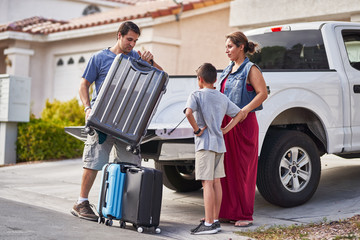 hispanic family packing luggage into pickup truck in front of house - obrazy, fototapety, plakaty