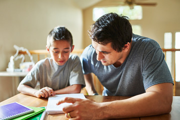 father helping son with homework on table at home