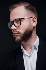 Stylish handsome bearded man with glasses in trendy suit on black background