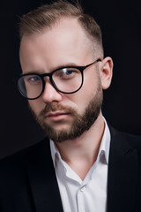 Stylish handsome bearded man with glasses in trendy suit on black background