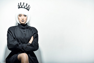 Black queen. A stern look. Black crown. A princess. Maleficent. Girl with a black crown decorated with precious stones sitting in studio on light background. Dark lipstick.