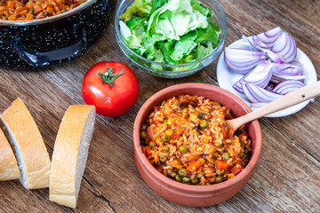 Fried rice with vegetables and spices in a vintage clay bowl and tomato, lettuce, onion and bread on wooden table