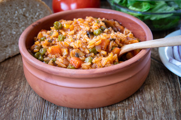 Fried rice with vegetables and spices in a vintage clay bowl and tomato, lettuce, onion and bread on wooden table