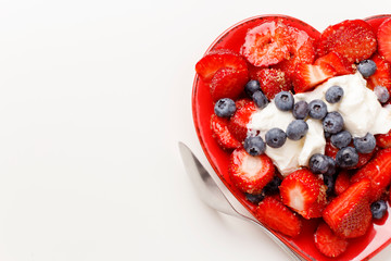 Mixed berries salad with yogurt and spoon on white background. Strawberry and blueberry on red heart plate.View from above. Copy space.
