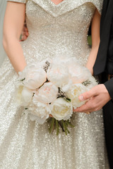 Bride and groom holding a bouquet of white peonies